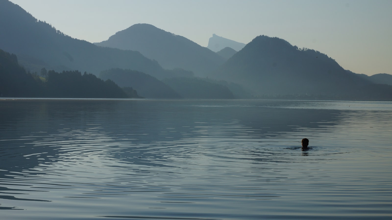 A lone swimmer in a calm still mountain lake with hills behind