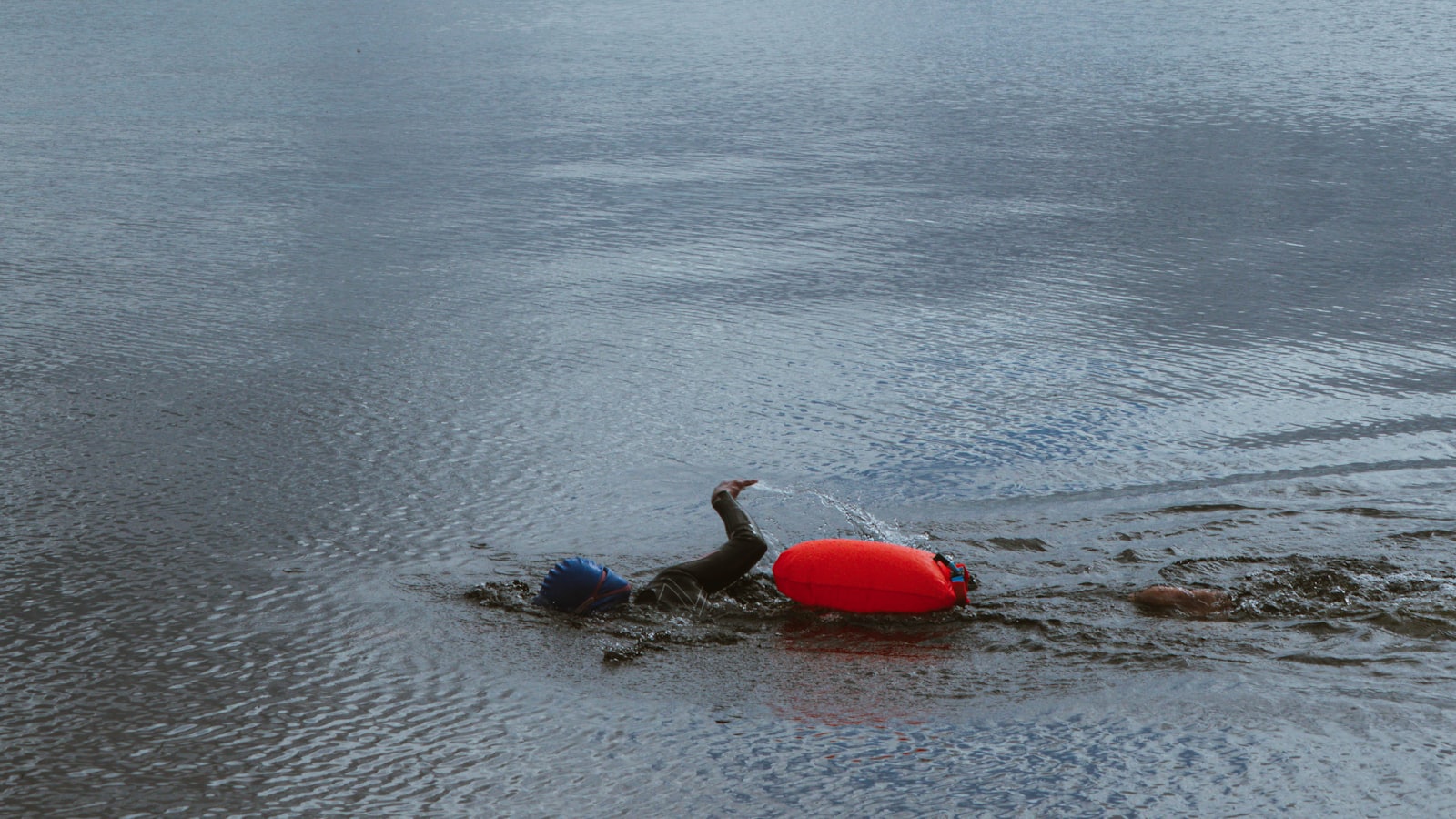 A swimmer with a bright orange tow float on a calm loch, mountains behind