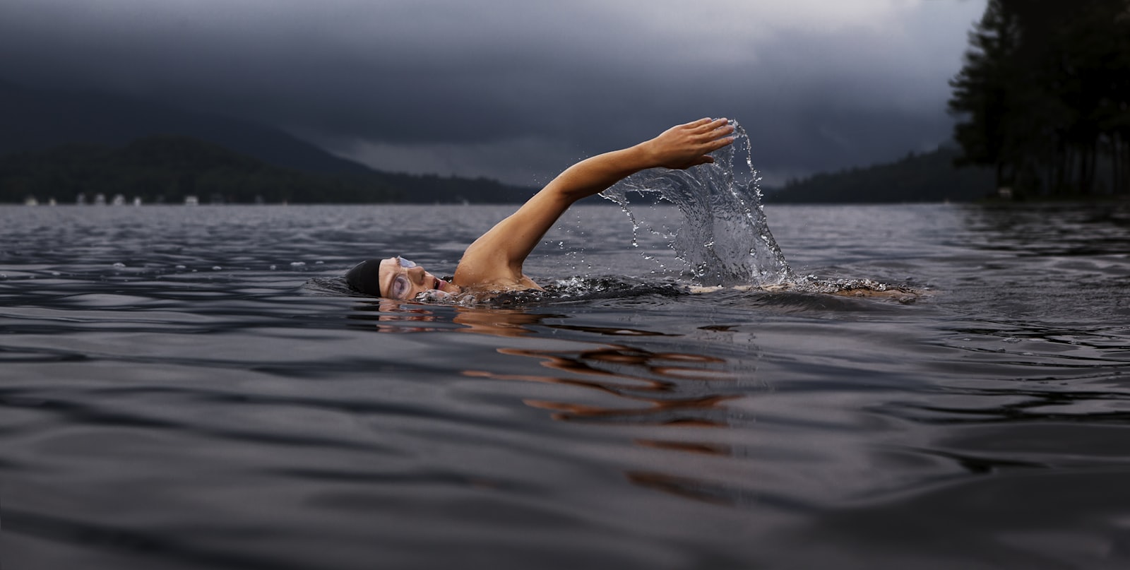A lone swimmer in still, open water beneath grey skies