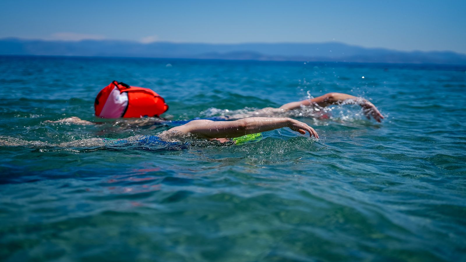 Open-water swimmers in a calm sea on a bright day