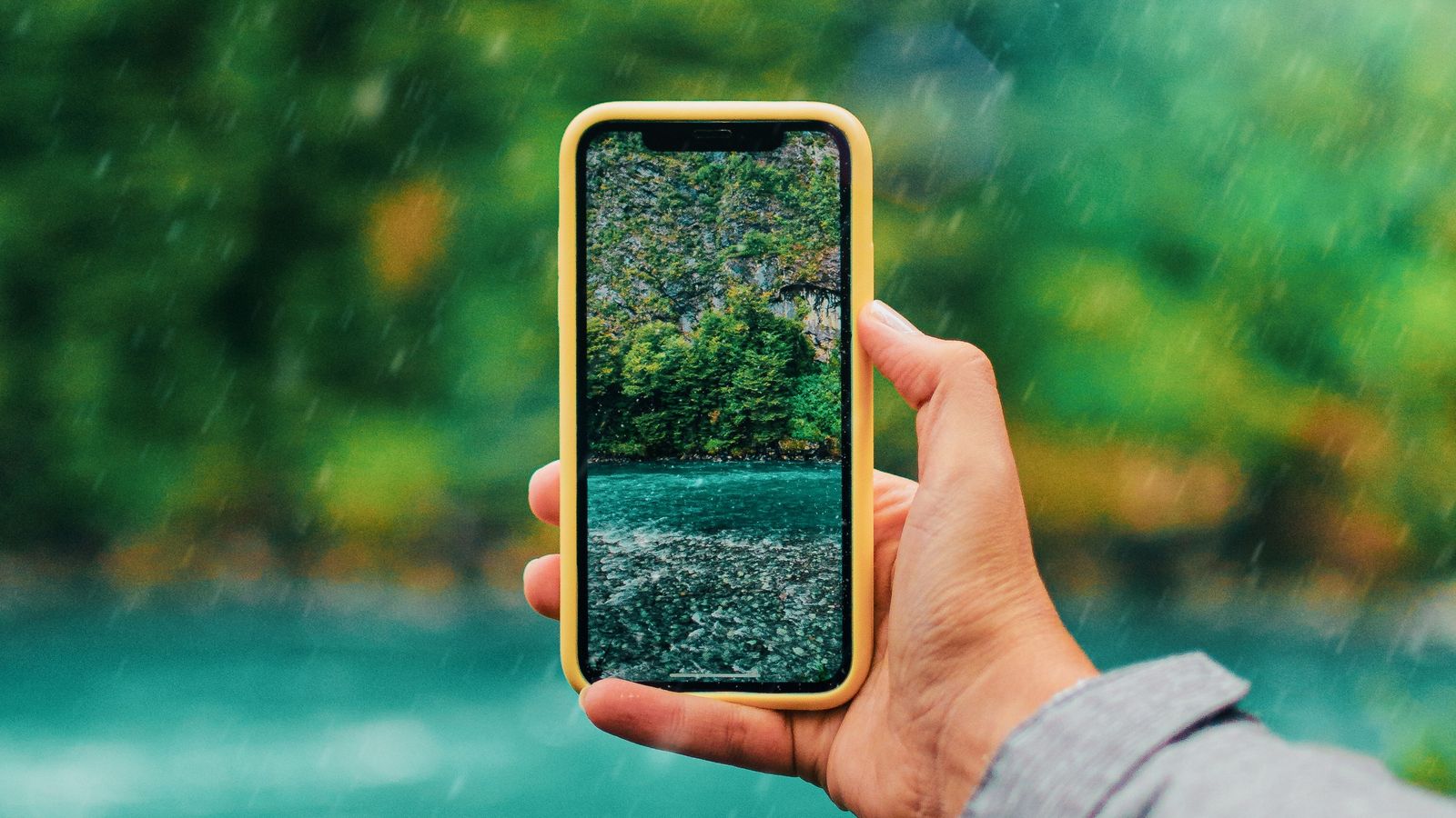 A hand holding a phone by a river
